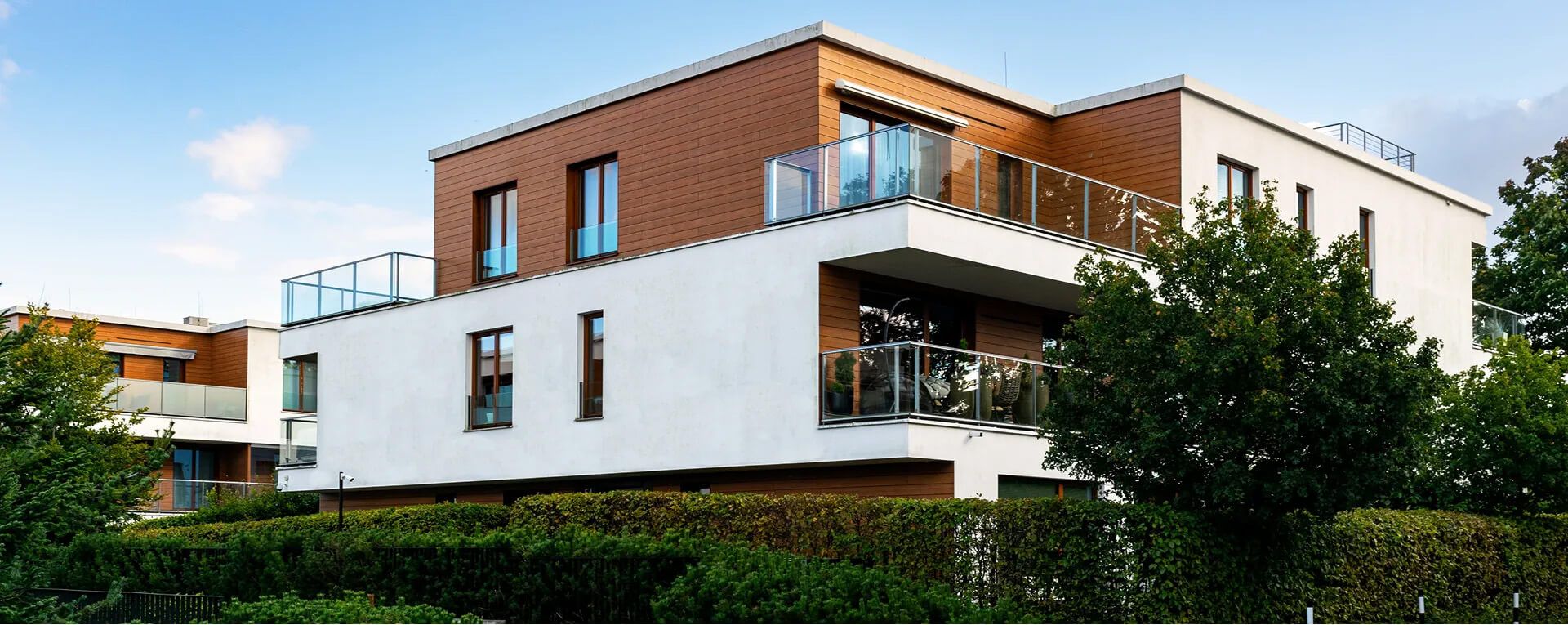 Modernes Wohngebäude mit mehreren Balkonen und großen Fenstern umgeben von Büschen und Bäumen